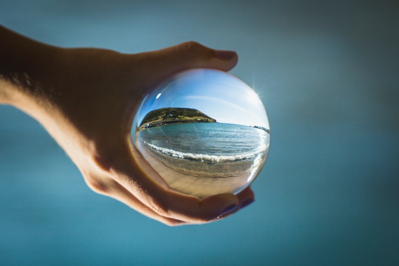 A hand holding a glass orb showing a beach view