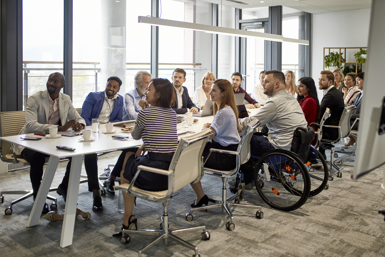 Comprehensive viewpoint of diverse group of business executives sitting together at conference table and looking at camera.